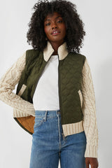 A woman wears a green quilted Veronica Beard Patra Jacket with cream knit sleeves, paired with a white t-shirt and blue jeans.
